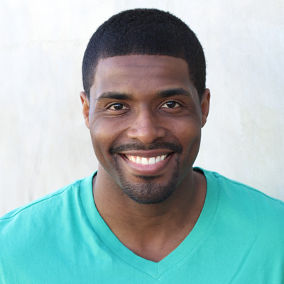 A man and woman are seated close together, smiling at the camera, with an open landscape in the background.